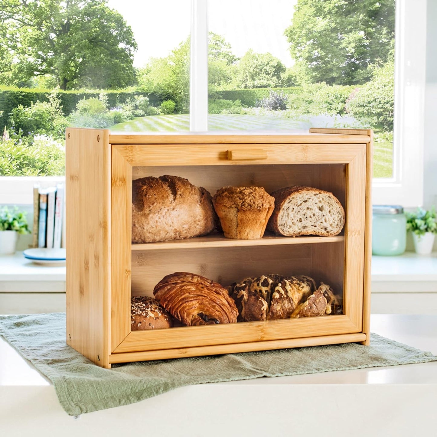 Wooden bread box with various types of bread on a windowsill with a garden view.