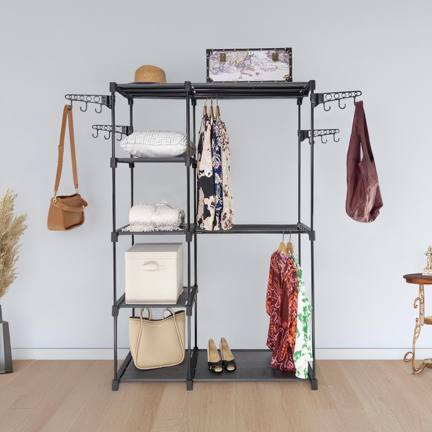 Black multi-tiered clothing rack with various items on a light wooden floor and light gray wall background.