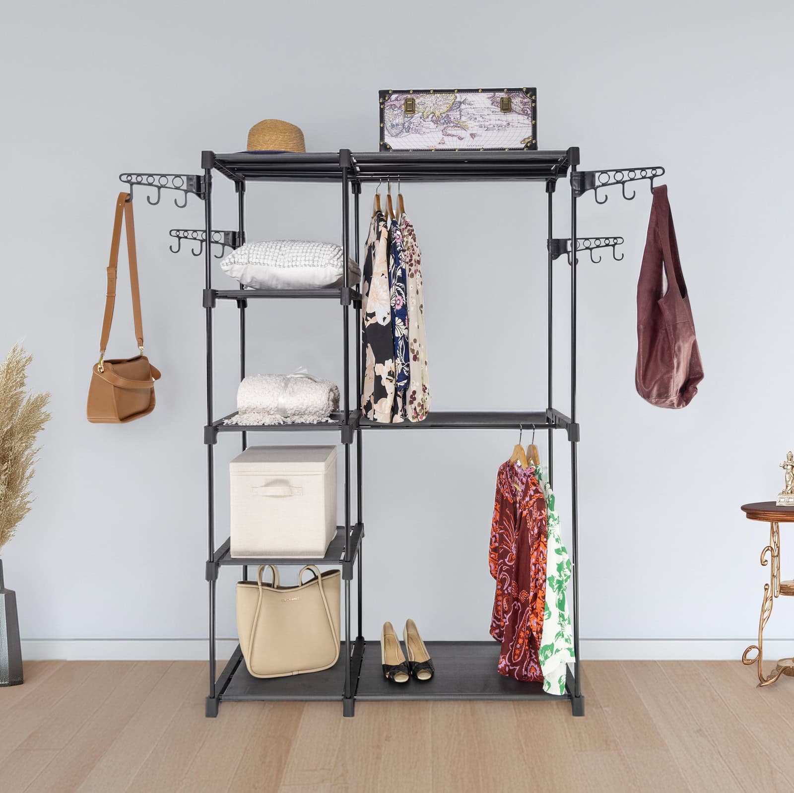 Black multi-tiered clothing rack with various items on a light wooden floor and light gray wall background.